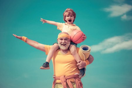 Téléchargez les photos : Grand-père sportif et enfant en bonne santé avec ballon de basket sur fond bleu ciel. Sport pour les petits enfants. Différentes générations - en image libre de droit