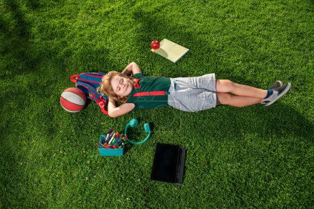 Foto de Un chico de escuela en la naturaleza. Alumno nerd. El niño está acostado en la hierba. Sueña con estudiar en la escuela. Niño feliz relajándose en la hierba - Imagen libre de derechos