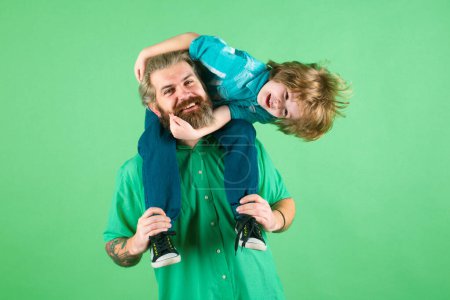 Photo for Fathers day. Father giving piggyback ride to his son against a green studio background. Happy family. Cute child boy hugs his daddy - Royalty Free Image