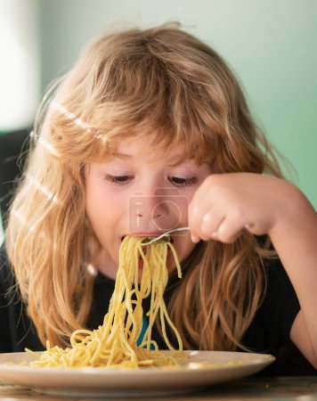 Téléchargez les photos : Tasty food, messy child eating spaghetti. Young kid sitting on the table eating healthy food with funny expression on face - en image libre de droit