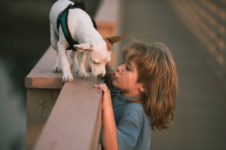 Foto de Lindo niño con cachorro. El niño besa al perro. Amistad, cuidado de mascotas, felicidad concepto de infancia - Imagen libre de derechos