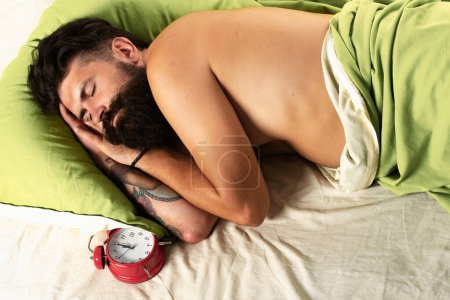 Foto de Hombre acostado en la cama y durmiendo. Hombre barbudo hipster teniendo problemas con el sueño. Hombre barbudo durmiendo en la cama en el dormitorio. Concepto de alarma - Imagen libre de derechos