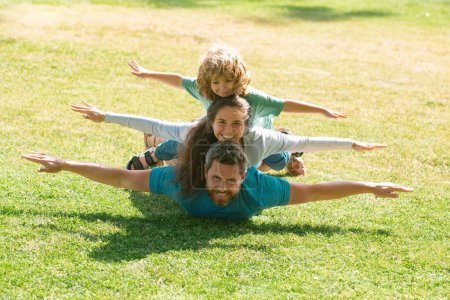 Photo for Family lying on grass in park. Parents giving child piggybacks in countryside - Royalty Free Image