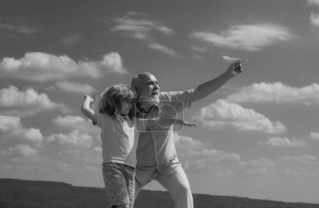 Foto de Abuelo e hijo jugando con el avión de papel sobre el cielo azul y las nubes de fondo - Imagen libre de derechos