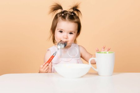 Photo for Baby child eating food. Good appetite. Baby with spoon on studio, isolated on beige yellow - Royalty Free Image