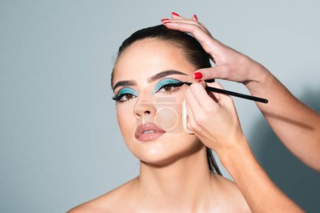 Beautiful woman face with perfect makeup. Makeup artist applies eye shadow. Hand of visagiste, painting cosmetics of young beauty model girl. Beauty girl with perfect skin