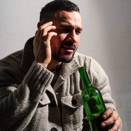 Téléchargez les photos : Un alcoolique avec des bouteilles de vin pleure. Un homme déprimé pleurant. Les hommes ivres buvant de l'alcool se sentent seuls et désespérés dans le stress émotionnel - en image libre de droit