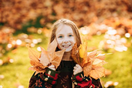 Téléchargez les photos : Adorable petite fille avec des feuilles d'automne dans le parc de beauté. Joyeux enfant fille riant et jouant feuilles en automne à l'extérieur. Enfants heureux jouant dans le parc d'automne - en image libre de droit