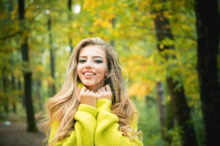 Foto de Hermosa joven feliz chica con la hoja de color rojo-amarillo brillante en el parque. Hermosa mujer de moda en vestido rojo de otoño con hojas que caen sobre el fondo de la naturaleza. Chica soñadora con el pelo largo en suéter de punto - Imagen libre de derechos