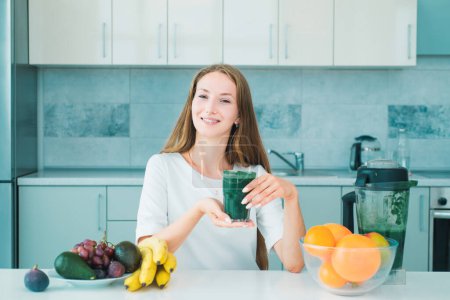 Photo for Well being and weight loss concept. Healthy Green food. Athletic young woman with protein shake in kitchen. Smiling healthy woman drinks green smoothie in kitchen - Royalty Free Image