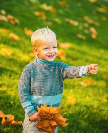Foto de Niño con hojas de otoño. Niño lindo en suéter chaqueta caliente en el fondo de la naturaleza de otoño. Concepto de infancia feliz. Niños en jersey de punto cálido - Imagen libre de derechos