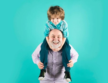 Photo for Grandfather and son piggyback ride with funny face isolated on blue in studio. Granddad and cute boy with funny face - Royalty Free Image