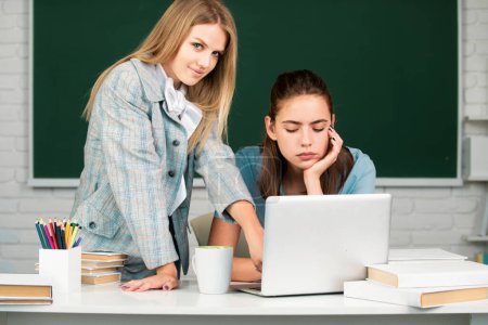 Photo for Students girls friends in classroom at school college or university on blackboard background. Two students looking at laptop computer doing homework together and helping each other - Royalty Free Image