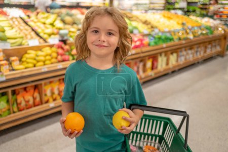 Foto de Niño eligiendo frutas y verduras durante las compras en el supermercado de verduras. Niño con limón y naranja. Un niño yendo de compras. Comida saludable para niños - Imagen libre de derechos