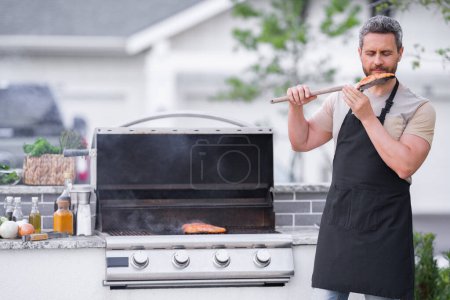 Photo for Man at barbecue grill. Male cook preparing barbecue outdoors. Bbq meat, grill for picnic. Roasted on barbecue. Man preparing barbeque in the house yard. Barbecue and grill. Cook using barbeque tongs - Royalty Free Image