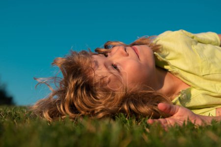 Téléchargez les photos : Des enfants rêvent. Joyeux petit garçon étendu sur l'herbe. Un rêve d'été. Des rêves d'enfant sur l'herbe. Rêve d'enfance. Enfant rêveur. Rêves et imagination. Visage d'enfant rêveur - en image libre de droit