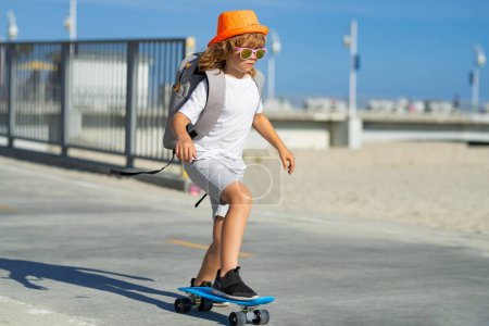 Téléchargez les photos : Enfants sportifs d'été avec skateboard. Enfant chevauchant skateboard sur la route. Un gamin qui pratique le skateboard. Les enfants apprennent à faire du skateboard dans un parc lors d'une journée ensoleillée d'été. Patinage pour enfants sur skateboards - en image libre de droit