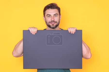 Photo for Happy guy with blank banner ad isolated on studio background. Portrait of smiling man holding empty blank poster. Man showing blank poster. Male presenting signboard, billboard or banner - Royalty Free Image