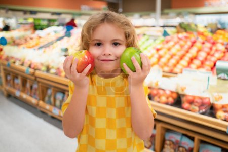 Téléchargez les photos : Un enfant tient des pommes à l'épicerie. Enfant choisissant des fruits et légumes pendant les achats au supermarché de légumes. Un gamin qui va faire du shopping. Aliments sains pour enfants - en image libre de droit