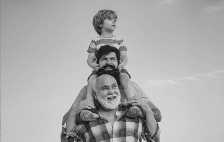Foto de Generación de hombres: el abuelo, el padre y el nieto se abrazan mirando a la cámara y sonriendo. Concepto del día de los padres. Concepto de generación. Juego familiar de fin de semana. Hombres en diferentes edades - Imagen libre de derechos