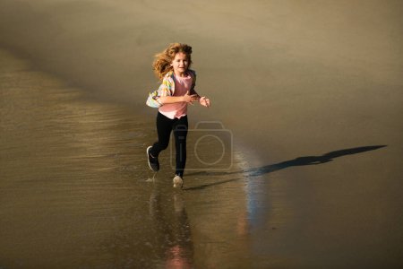 Téléchargez les photos : Un enfant court au bord de la mer. Des enfants qui courent sur la plage. Vacances d'été. Joyeux gamin jouant sur la plage. Bonne enfance. Course et sport sain pour les enfants - en image libre de droit
