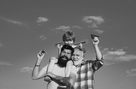 Foto de Piloto de niño con jetpack de juguete contra el fondo del cielo. Feliz tres generaciones de hombres se divierten y sonríen en el fondo del cielo azul. Niño feliz jugando al aire libre - Imagen libre de derechos