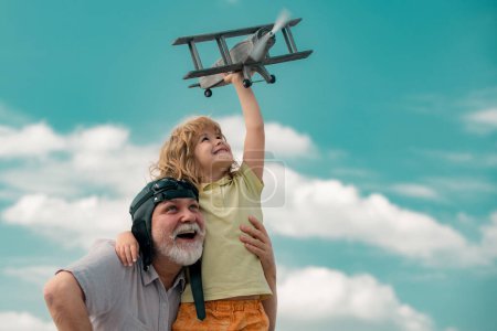 Téléchargez les photos : Vieux grand-père et jeune petit-fils enfant jouant avec un avion jouet sur fond de ciel d'été. Générations âges - en image libre de droit