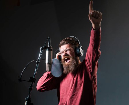 Foto de Cantante con cara de expresión usando auriculares está interpretando una canción con un micrófono mientras graba en un estudio de música - Imagen libre de derechos