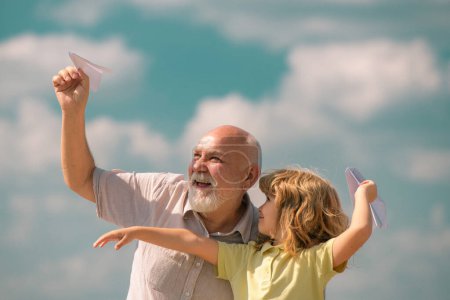 Photo for Grandson child and grandfather with paper plane over blue sky and clouds. Men generation granddad and grandchild - Royalty Free Image