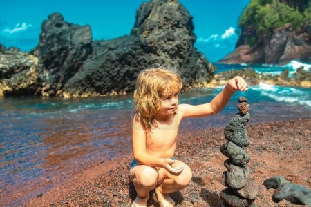 Foto de Niño lindo haciendo guijarros se apilan en una roca volcánica junto al mar. Concepto zen - Imagen libre de derechos