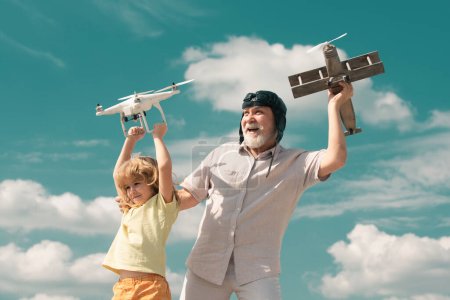 Photo for Young grandson and old grandfather hold plane and drone quad copter against sky. Child pilot aviator with plane dreams of flying. Family Relationship Grandfather and child - Royalty Free Image