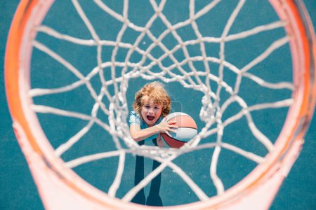 Téléchargez les photos : Vue du dessus de l'enfant excité jouant au basketball tenant le ballon avec le visage heureux - en image libre de droit
