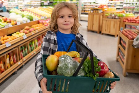 Téléchargez les photos : Enfant avec panier plein de légumes et de fruits. Un gamin dans un magasin d'alimentation. Supermarché et concept d'épicerie. Enfant avec panier - en image libre de droit