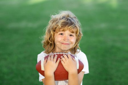 Téléchargez les photos : Football américain. Enfant avec football américain, ballon de rugby. Portrait mignon d'un footballeur américain - en image libre de droit