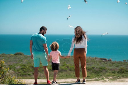 Photo for Back view of happy young family walking on beach. Child with parents holding hands. Full length freedom poeple - Royalty Free Image