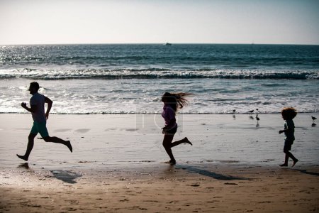 Téléchargez les photos : Silhouettes de famille fitness courant près de la mer. Jogging familial pour le sport pour la remise en forme en plein air avec enfant - en image libre de droit