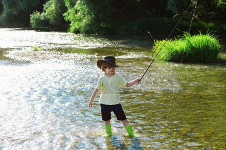Téléchargez les photos : Pêche d'enfant. Un gamin qui apprend à pêcher en tenant une canne sur une rivière. Petit garçon pêcheur avec canne à pêche. Jeune homme mouche pêche - en image libre de droit