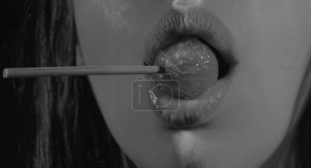 Photo for Lollipop in the mouth, close-up. Beautiful girl mouth with lolli pop. Glossy red woman lips with tongue. Mouth lick suck chupa chups on neon lights. Night club background - Royalty Free Image