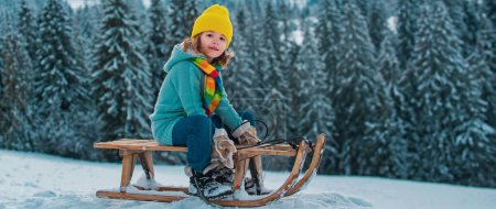 Photo for Kid boy having fun with a sleigh on winter landscape. Cute children playing in a snow on snowy nature landscape. Winter activities for kids - Royalty Free Image