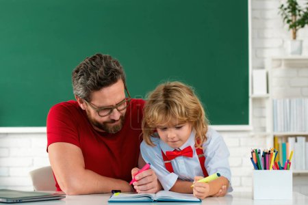 Photo for Kid boy learning with teacher. Funny little boy study with father in class on blackboard. Child from elementary school. Elementary school boy in classroom on lesson. Teacher explaining to pupil - Royalty Free Image