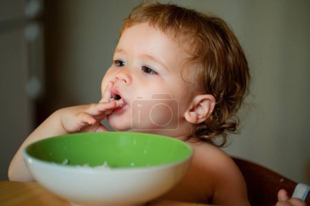 Photo for Happy baby eating himself with a spoon. Healthy nutrition for kids. Baby holding a spoon while putting it in his mouth - Royalty Free Image