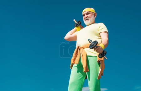 Photo for Senior sportman exercising with lifting dumbbell on blue sky background. Isolated, copy space. Portrait of senior man holding dumbbell. Healthcare cheerful lifestyle - Royalty Free Image