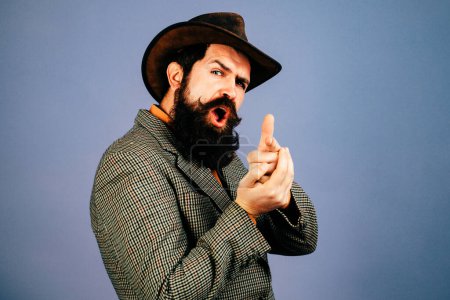 Photo for Bearded man holds imaginable gun in his hands and looks at the camera. Hand with fingers set into gun gesture. Symbolizing shooting someone - Royalty Free Image