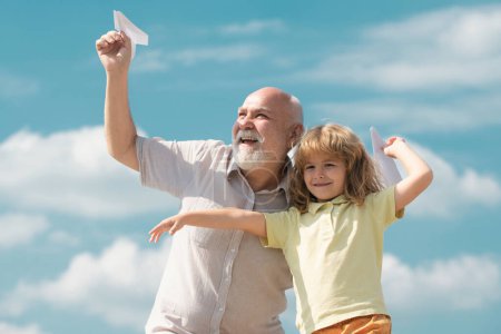Téléchargez les photos : Grand-père et fils jouant avec jouet avion en papier sur fond de ciel d'été. Enfant garçon rêvant de voler. Relations familiales Grand-père et enfant - en image libre de droit