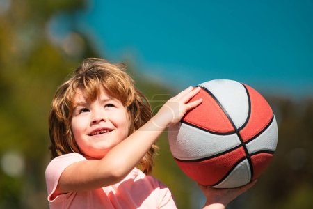 Foto de Lindo niño jugando baloncesto. Lindo chico sonriente juega basket ball. Niños activos disfrutando al aire libre juego - Imagen libre de derechos
