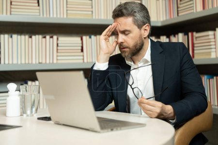 Photo for Millennial Businessman in office having headache. Business man in suit work on laptop at home office take off glasses suffer from migraine or headache. Tired exhausted man suffering from headache - Royalty Free Image