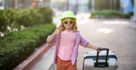 Foto de Niño turista viajero en ropa casual, gafas de sol de moda y sombrero sostienen maleta. Los niños viajan y viajan fin de semana. Viaja al extranjero los fines de semana. Viaje de niños - Imagen libre de derechos