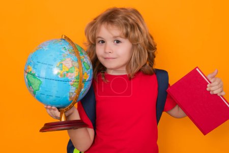 Téléchargez les photos : School kid hold world globe and book. Back to school. Funny little student boy from elementary school with book. Pupil on studio isolated background - en image libre de droit