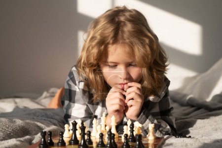 Téléchargez les photos : Intelligent enfant pensant. Un gamin joue aux échecs. Enfant pensant. Jeu d'échecs pour les enfants. Intelligent, intelligent et intelligent garçon d'école - en image libre de droit