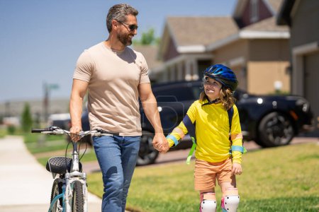 Téléchargez les photos : Père enseignant fils à vélo. Père aidant fils excité à faire du vélo dans le quartier américain. Enfant en casque de vélo apprenant à faire du vélo avec son père. Fête des pères - en image libre de droit